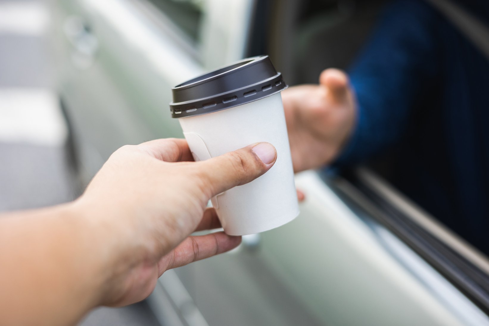 Drive thru coffee. Young buying a cup of hot coffee while driving the vehicle. Take a break for a refreshing coffee before your trip.